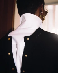 Close-up back view of a person wearing a black jacket over a white high-collar shirt with gold buttons for Celine 2026.