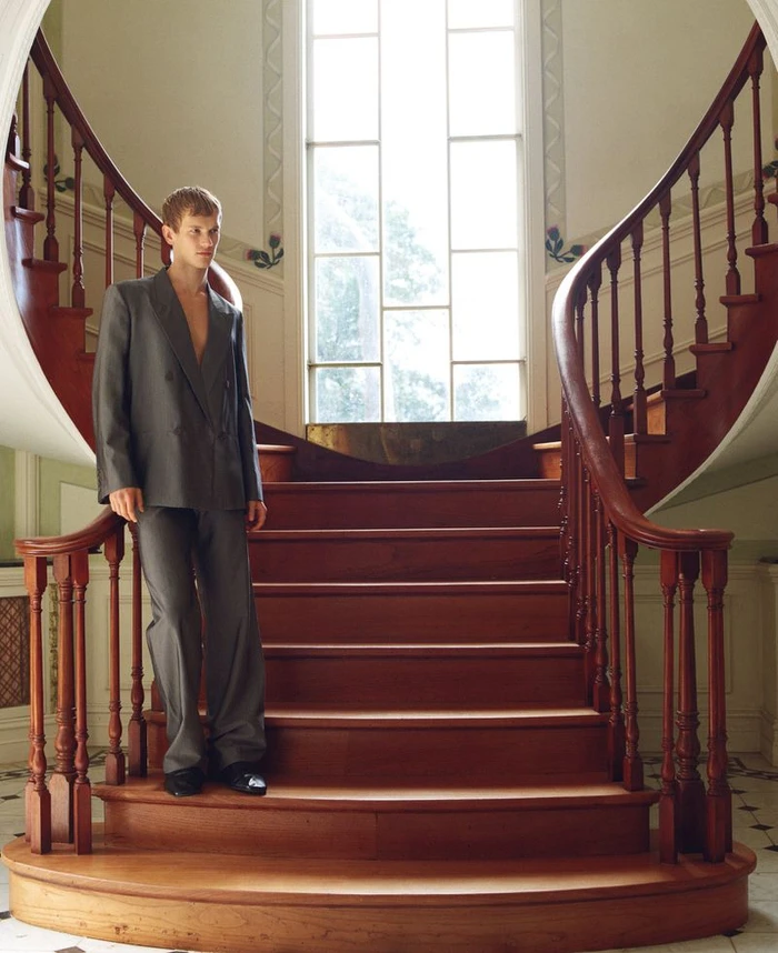 Model Max Tate standing on a curved wooden staircase wearing a grey suit jacket and trousers for GQ Australia