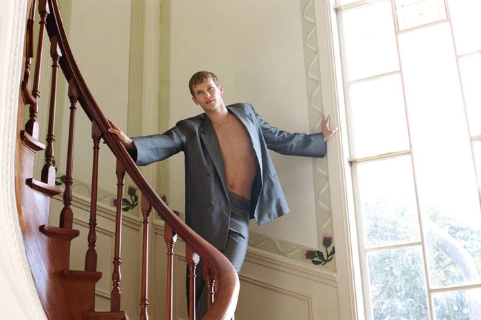 Model Max Tate standing on wooden stairs in an oversized grey suit jacket for GQ Australia by Rob Tennent