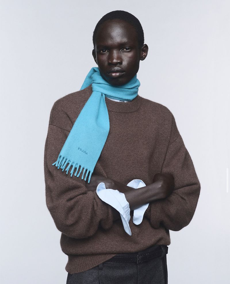 Model wearing a brown wool sweater and a bright blue scarf against a plain white studio background.