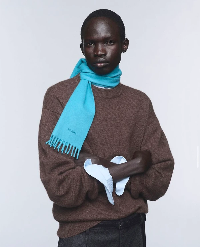 Model wearing a brown wool sweater and a bright blue scarf against a plain white studio background.