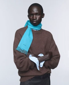 Model wearing a brown wool sweater and a bright blue scarf against a plain white studio background.