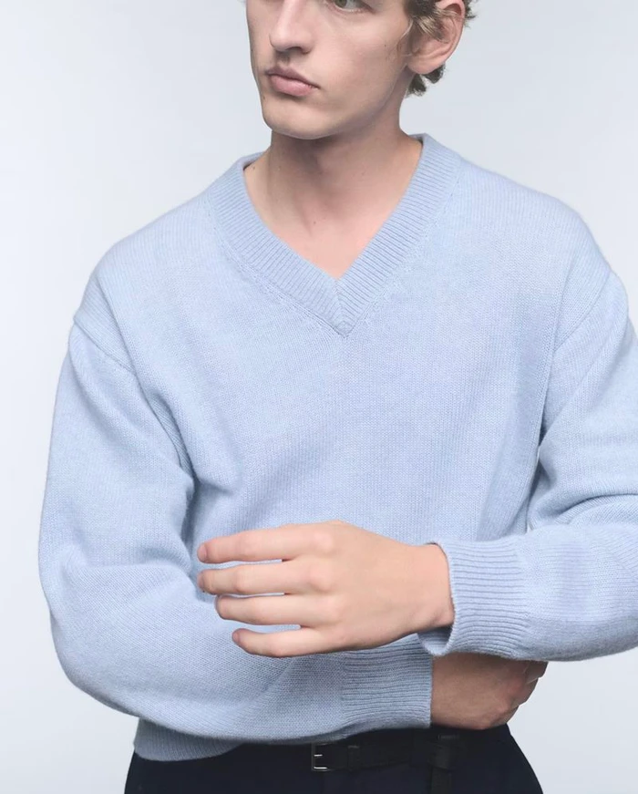 Man wearing a light blue v-neck cashmere sweater against a neutral background for Prada