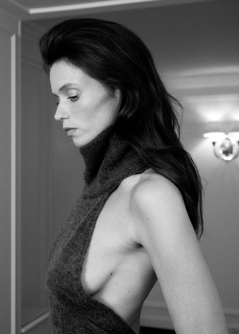 Model Abbey Lee in a dark turtleneck sleeveless top captured in profile against a soft indoor background.