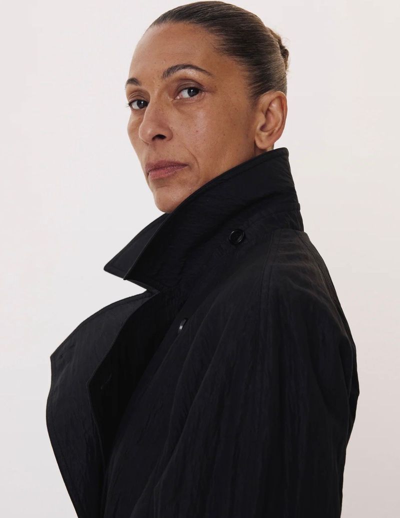 Profile portrait of a woman wearing a black trench coat against a plain white background for Recto F/W 26