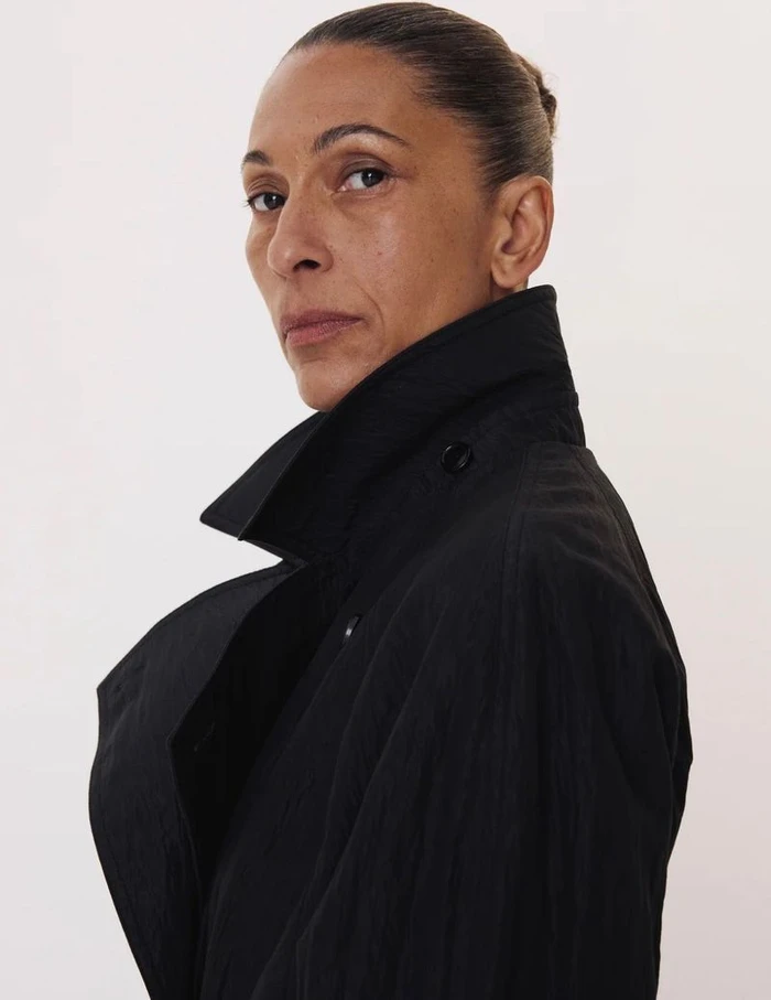 Profile portrait of a woman wearing a black trench coat against a plain white background for Recto F/W 26