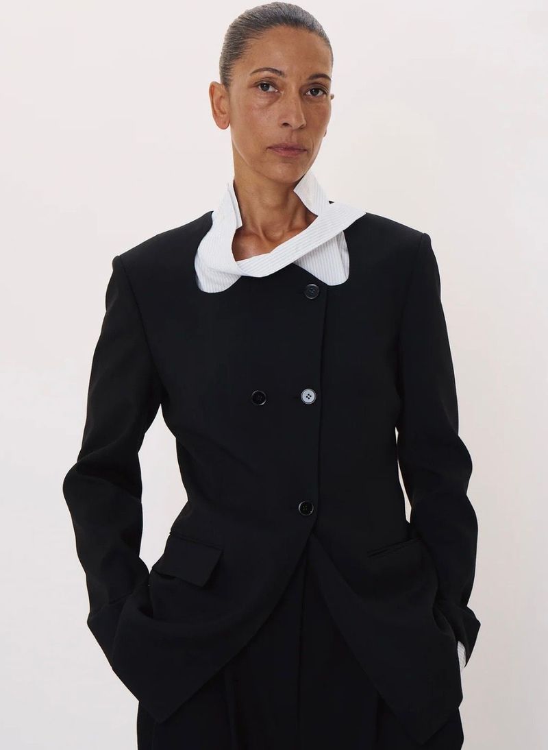 Model in a black blazer with an asymmetrical white collar against a plain white studio background