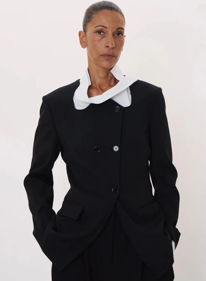 Model in a black blazer with an asymmetrical white collar against a plain white studio background