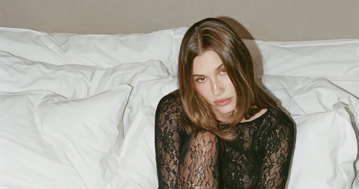 Hailey Bieber wearing a black lace top seated against white pillows for a Calzedonia campaign