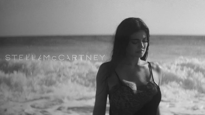 Kylie Jenner in a black slip dress standing on a sandy beach by the ocean for Stella McCartney Wild Horses