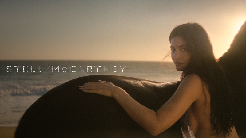 Kylie Jenner resting her hand on a horse at sunset on a sandy beach for Stella McCartney