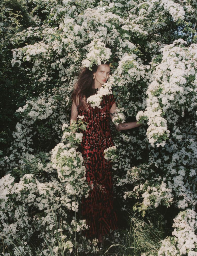 Model Waleska Gorczevski in a patterned red and black dress standing among dense white blossoming bushes for Numero Netherlands.
