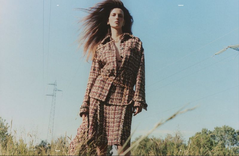 Model Waleska Gorczevski in a plaid tweed jacket and skirt standing outdoors against a blue sky with power lines for Numero Netherlands