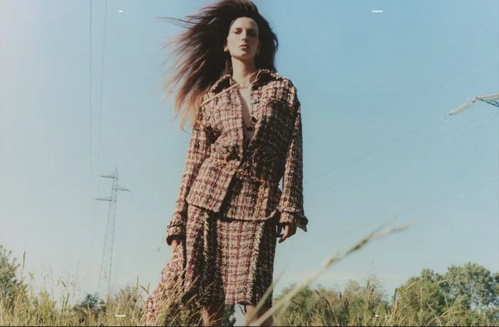 Model Waleska Gorczevski in a plaid tweed jacket and skirt standing outdoors against a blue sky with power lines for Numero Netherlands