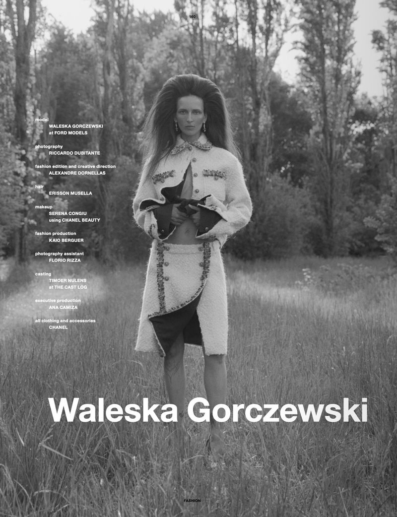Model Waleska Gorczevski standing in a tall grassy field wearing a textured white jacket and skirt set in a black and white editorial photo.