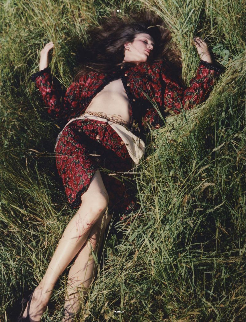 Model Waleska Gorczevski lying in tall green grass wearing a patterned red and black patterned skirt suit