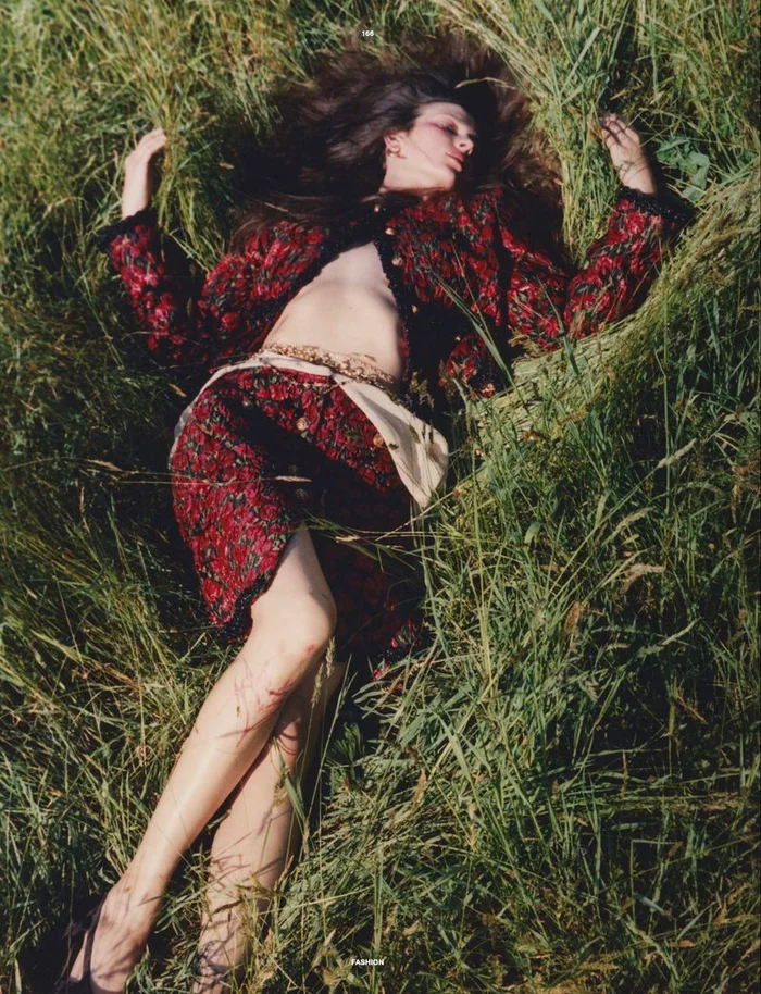 Model Waleska Gorczevski lying in tall green grass wearing a patterned red and black patterned skirt suit