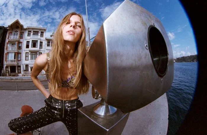 Model Karen Waage in black leather trousers leaning against a metal periscope structure by the waterfront for Num&eacute;ro Istanbul.