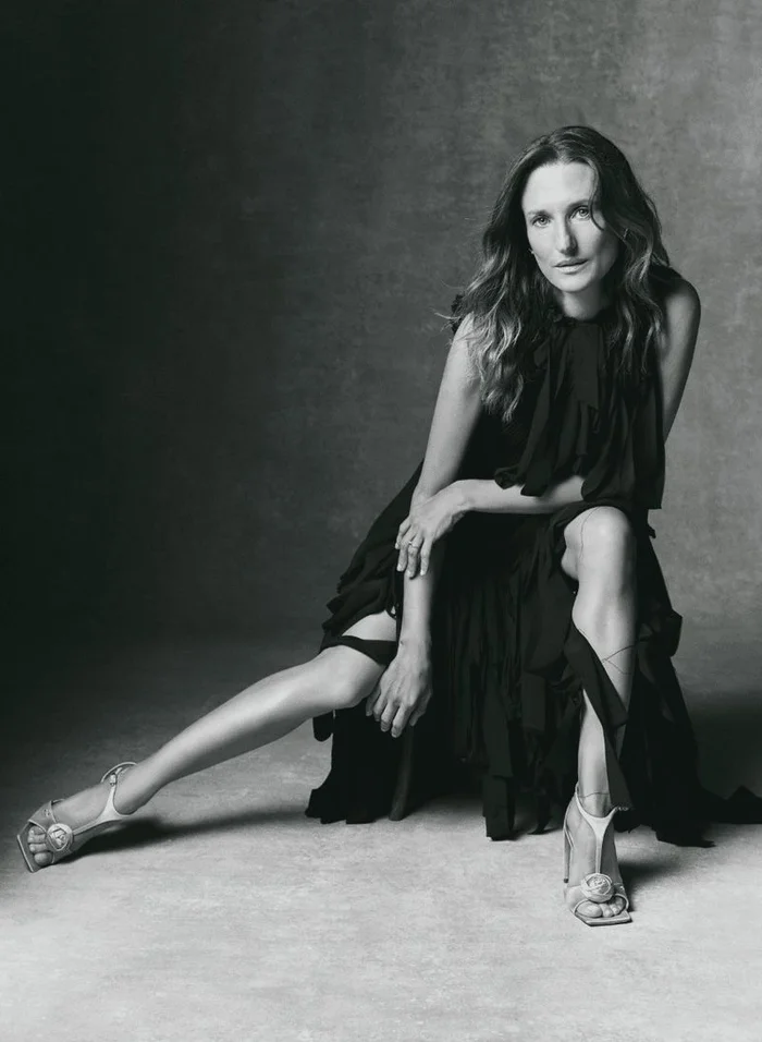 Camille Cottin seated in a black ruffled dress against a textured grey background for Vanity Fair France.