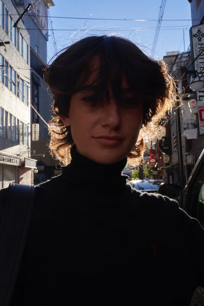 Model with dark hair wearing a black turtleneck sweater standing on a city street.