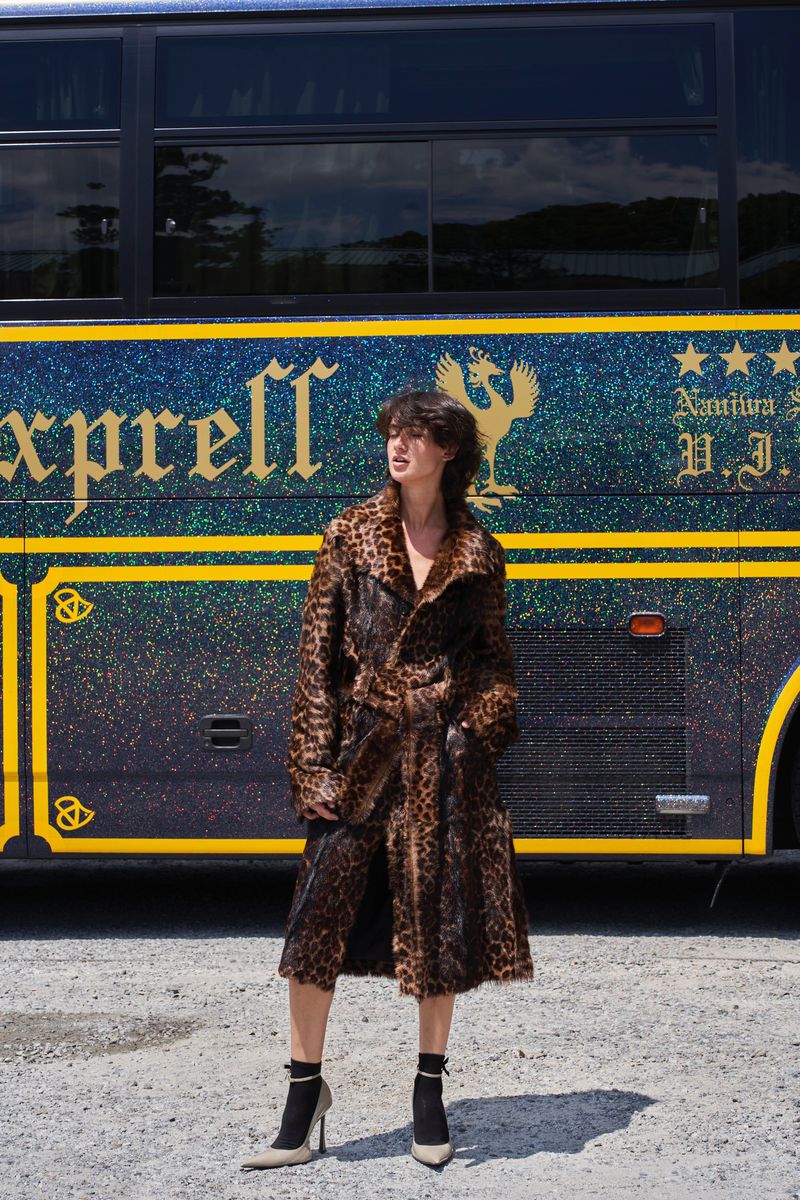 Model wearing a leopard print coat standing in front of a dark bus with gold lettering for ODDA Magazine editorial.