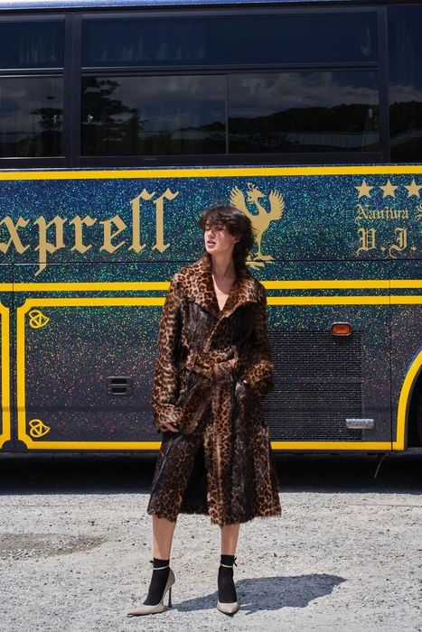 Model wearing a leopard print coat standing in front of a dark bus with gold lettering for ODDA Magazine editorial.