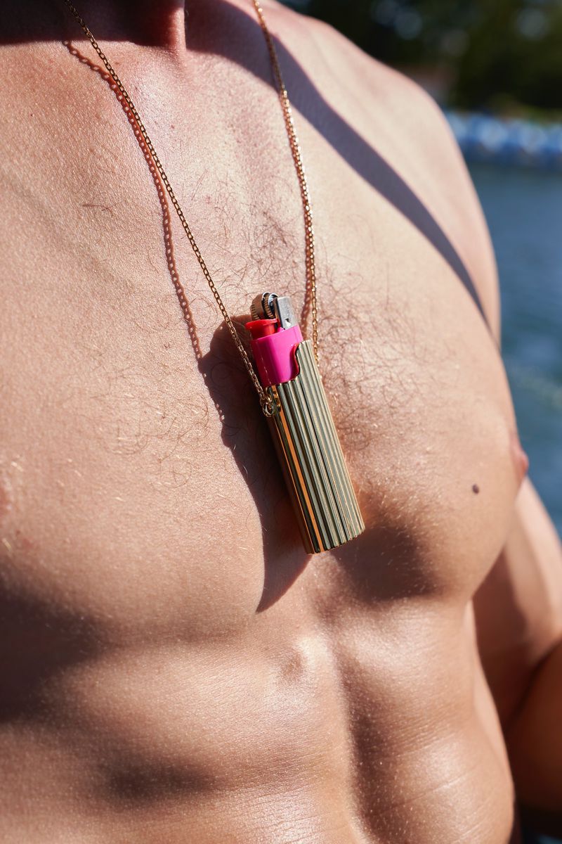 Close-up of a shirtless man wearing a gold chain necklace with a lighter pendant for ODDA Magazine