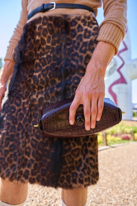 Close-up of a person wearing a leopard print skirt, tan sweater, and holding a dark handbag for ODDA Magazine editorial