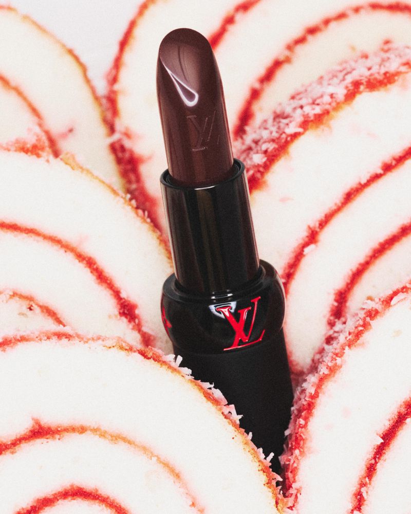 Dark lipstick tube with LV logo positioned vertically amidst sliced white and red patterned sponge cake rolls