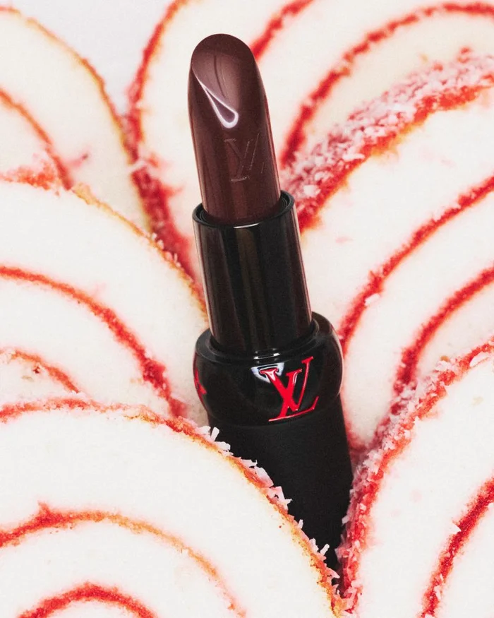Dark lipstick tube with LV logo positioned vertically amidst sliced white and red patterned sponge cake rolls