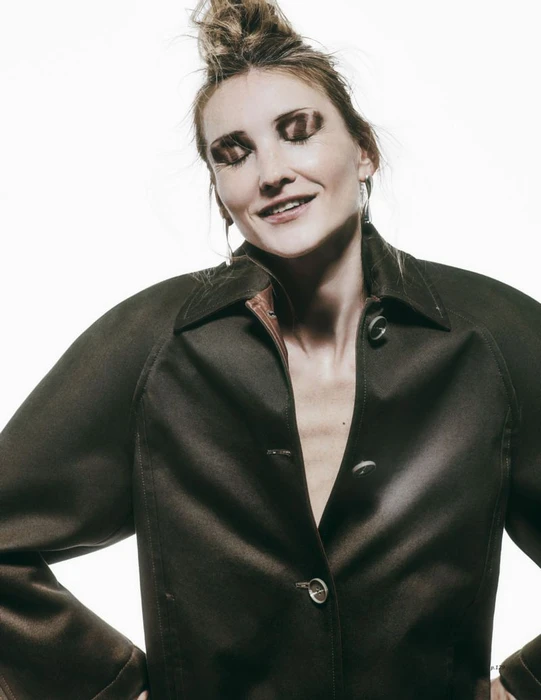 Model wearing a dark brown buttoned jacket with hair up in a top knot against a clean white background.