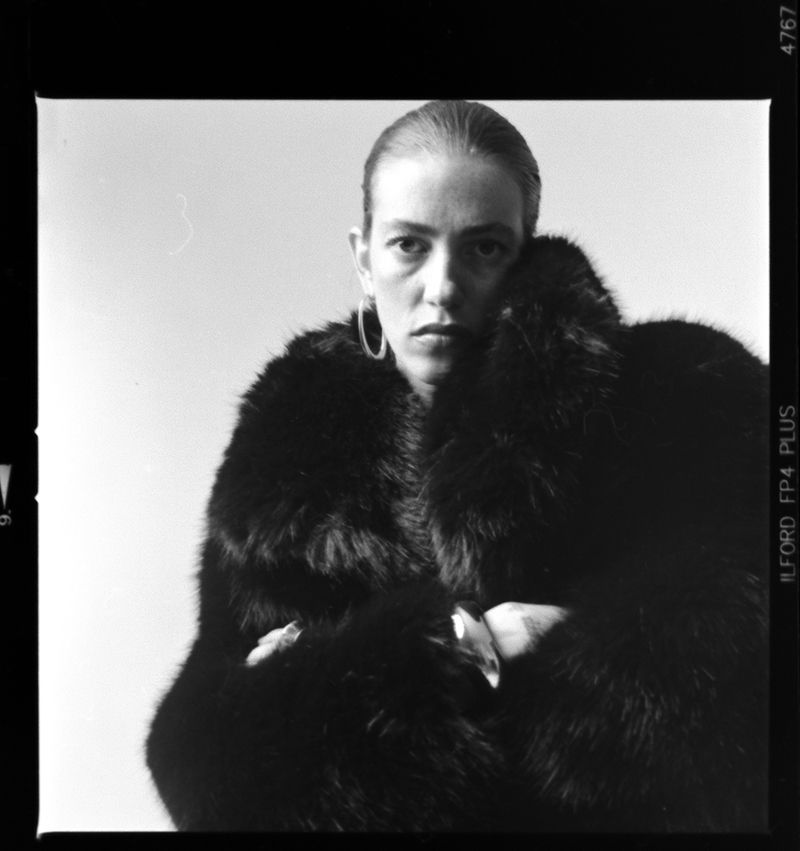 Black and white portrait of a woman with hoop earrings and a dark fur coat against a stark white backdrop, shot on film.