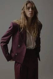 Model wearing a deep burgundy blazer and trousers against a neutral grey studio backdrop