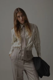Model in striped shirt and patterned tie holding a dark jacket against a grey background