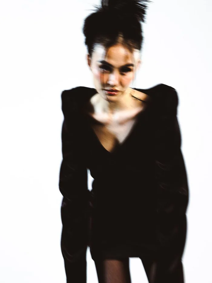Agnez Mo in a dark V-neck dress with styled hair against a plain white background for Schön Magazine, photographed by Joelle Grace Taylor