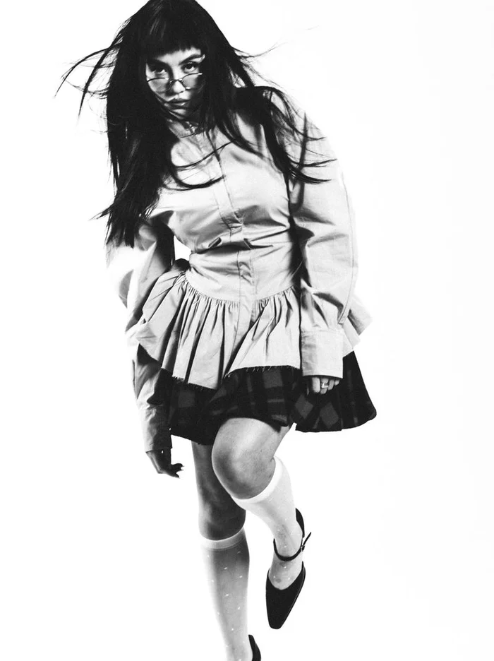Model with dark hair in glasses wearing a buttoned top and skirt against a bright white background for Schön Magazine.