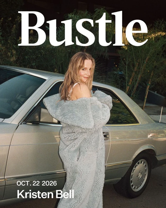 Kristen Bell wearing a long grey coat leaning against a silver car for Bustle Magazine