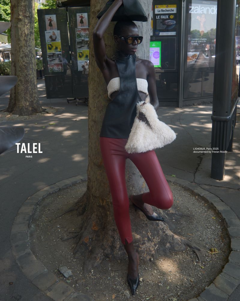 Fashionable woman poses in a black halter top, red leggings, sunglasses and a purse while standing near a tree on a city street.