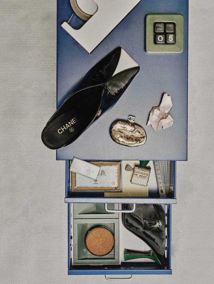 Top-down view of a blue metal cabinet with drawers, displaying Chanel shoes, a metallic purse, and stationery for L'Officiel Italia.