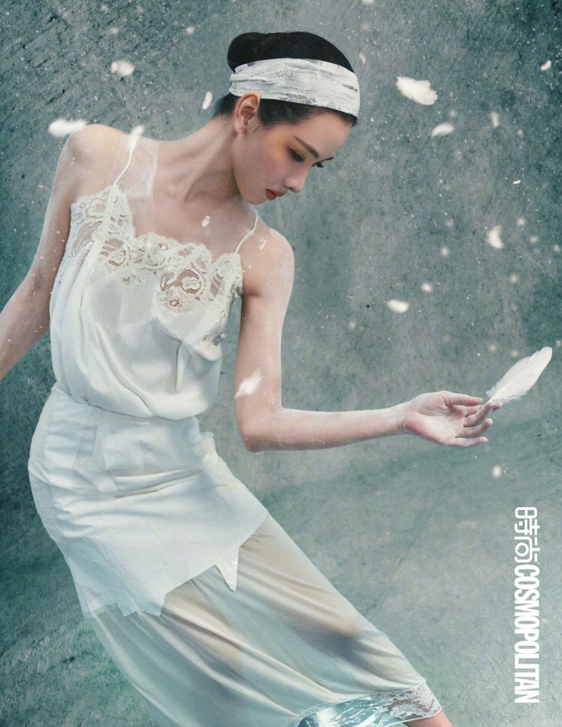 Chen Duling in a white lace camisole and skirt holding a white feather amidst floating feathers against a grey textured background.