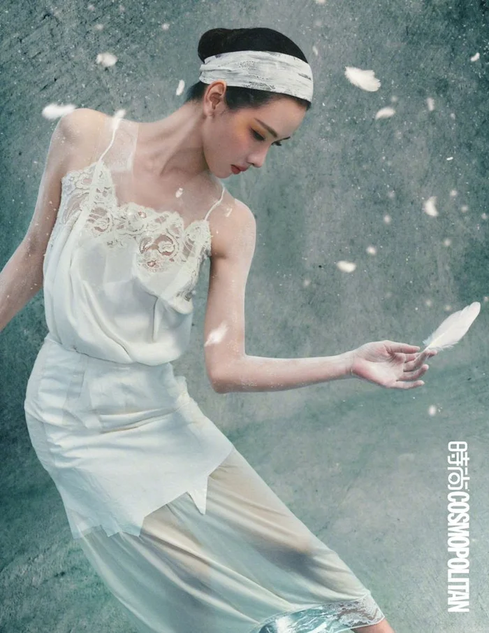 Chen Duling in a white lace camisole and skirt holding a white feather amidst floating feathers against a grey textured background.