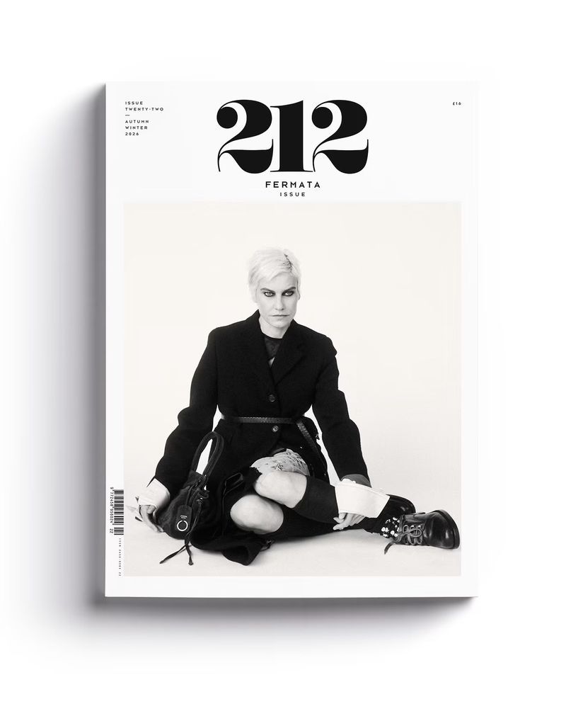 Magazine cover featuring a seated model in a black jacket and boots against a white studio background.