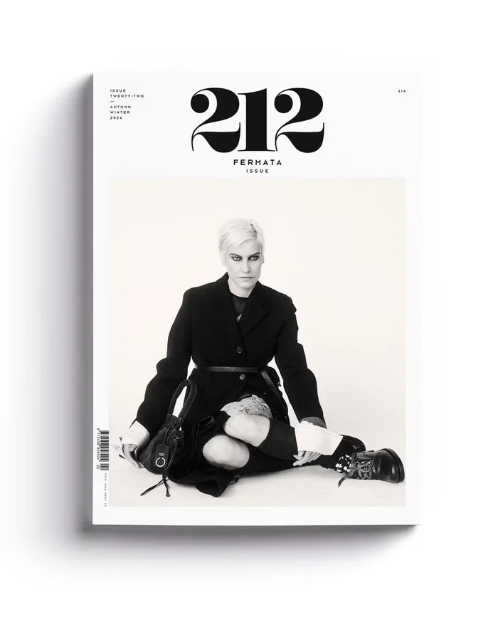 Magazine cover featuring a seated model in a black jacket and boots against a white studio background.