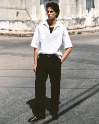 Model standing on a paved street wearing a white short-sleeve polo shirt and dark trousers for COS