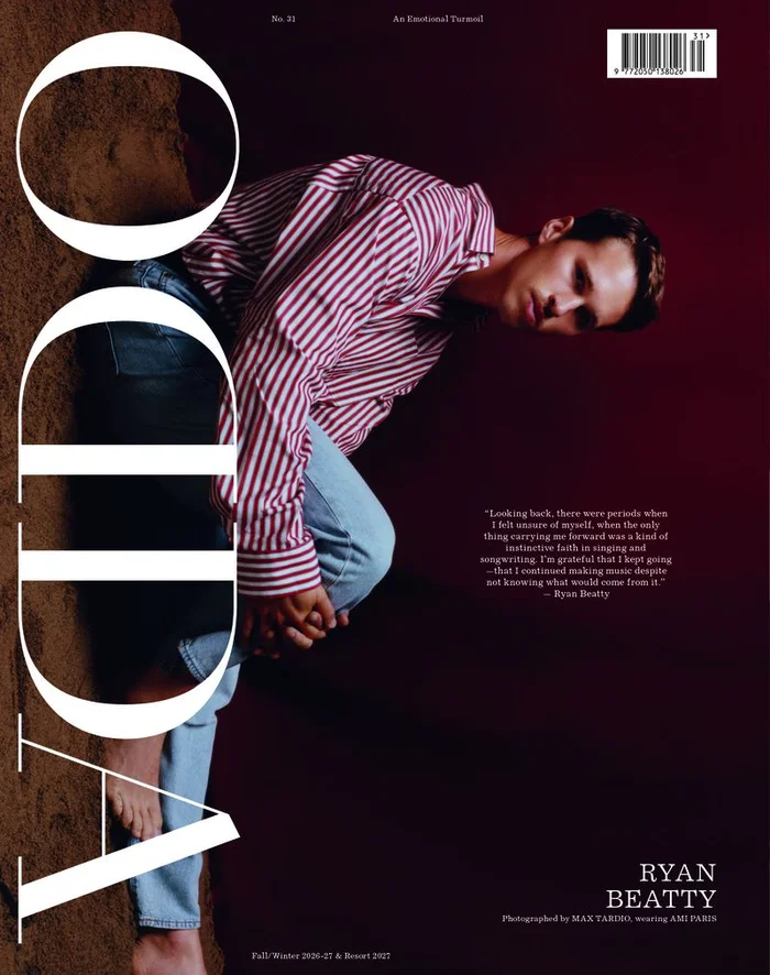 A man in a red and white striped shirt and blue jeans poses against a dark background with large white typography.
