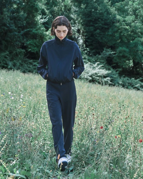 Meadow Walker walking through a wildflower meadow wearing a dark navy athletic tracksuit by Jil Sander and Puma