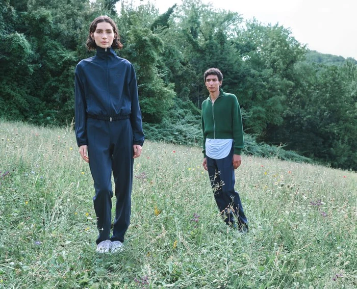 Two models standing in a grassy meadow wearing dark blue and green athletic tracksuits for Jil Sander and Puma AW26 collection.
