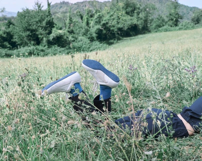 Person lying in a lush grassy meadow with legs elevated showing white sneakers with blue soles and blue socks