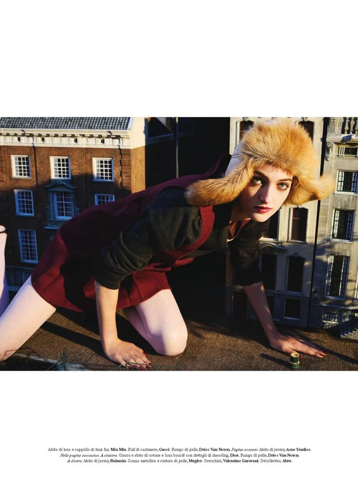 Model Frauke Nijs wearing a fluffy faux fur trapper hat and burgundy outfit posing over a miniature building model