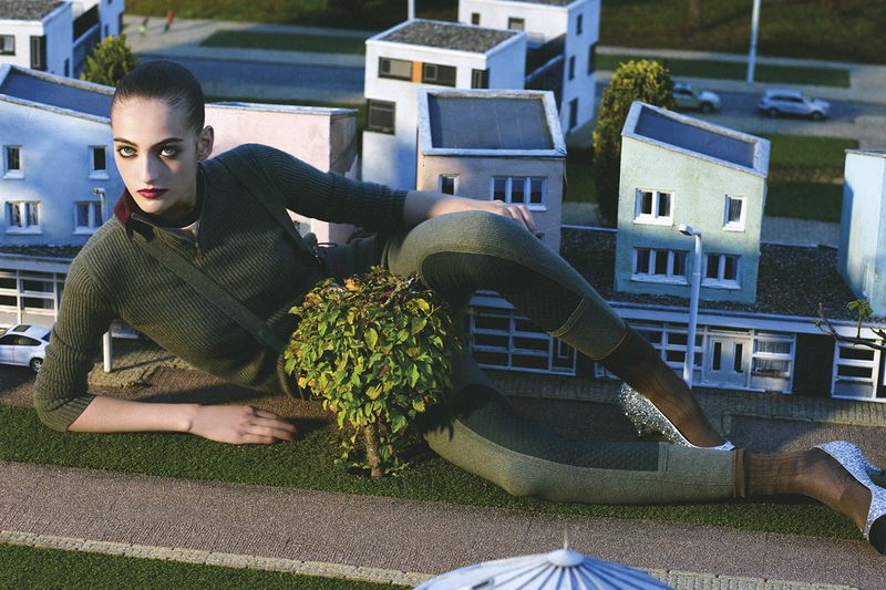 Model Frauke Nijs in olive green knitwear posing over a miniature town model for D Repubblica